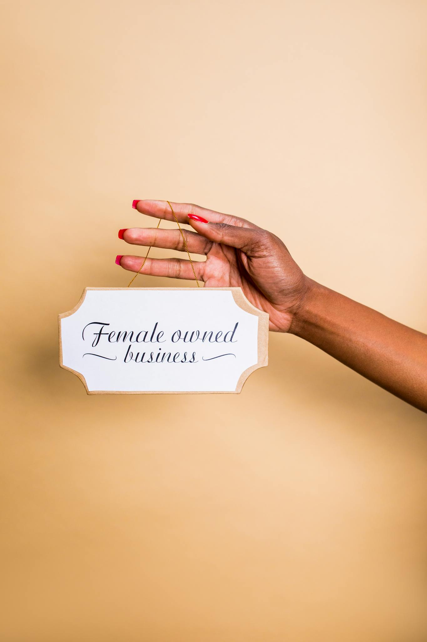 Close-up of a hand holding a female-owned business sign on a brown background.