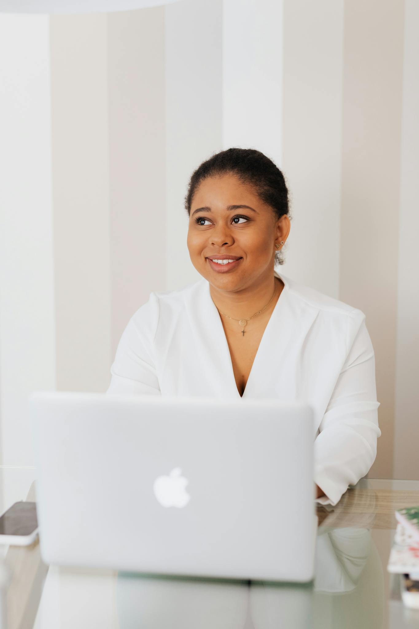 Smiling woman in a white top using a laptop in a modern, bright office setting.
