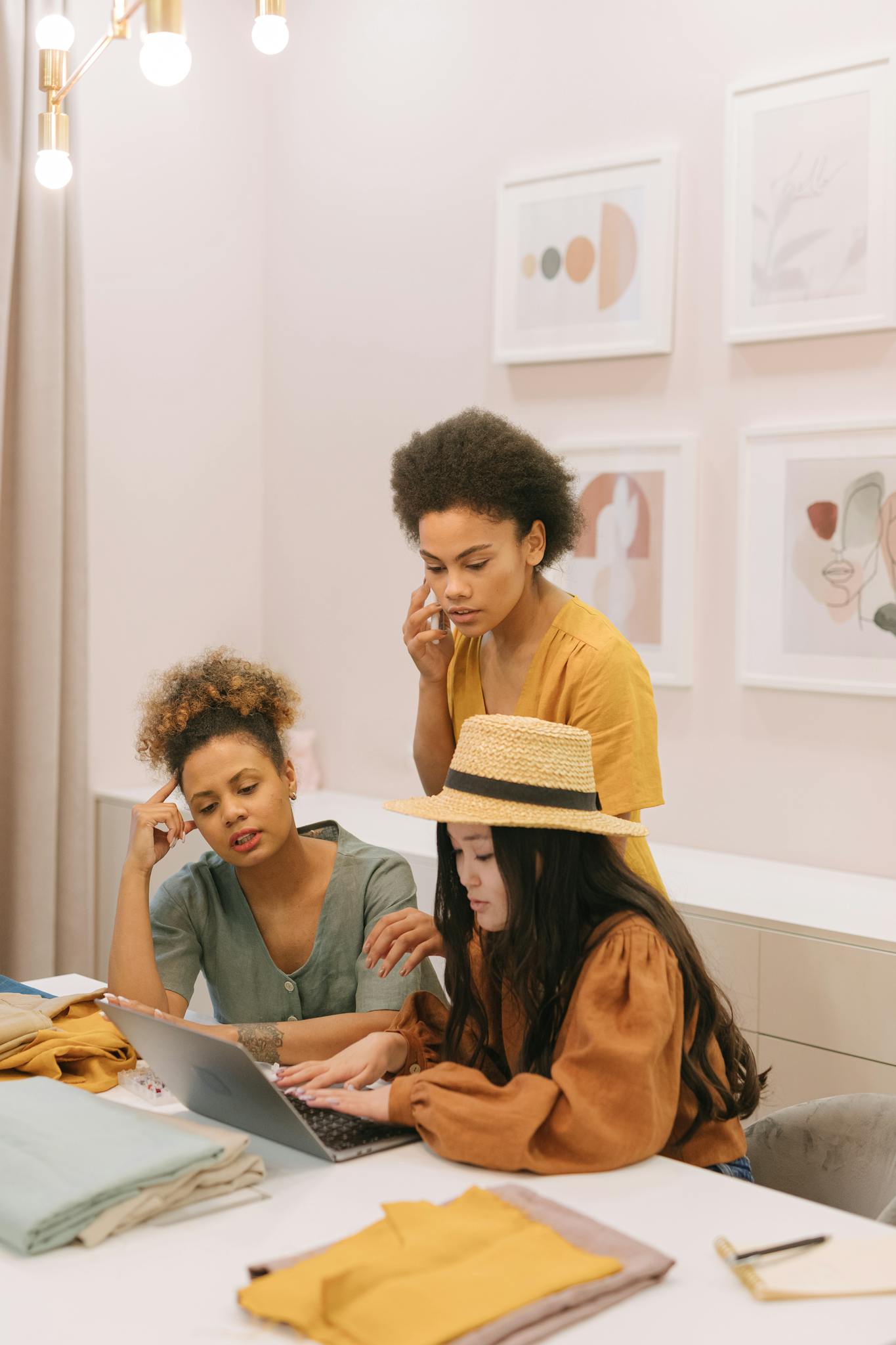 Three women working together on a laptop in a creative office setting.