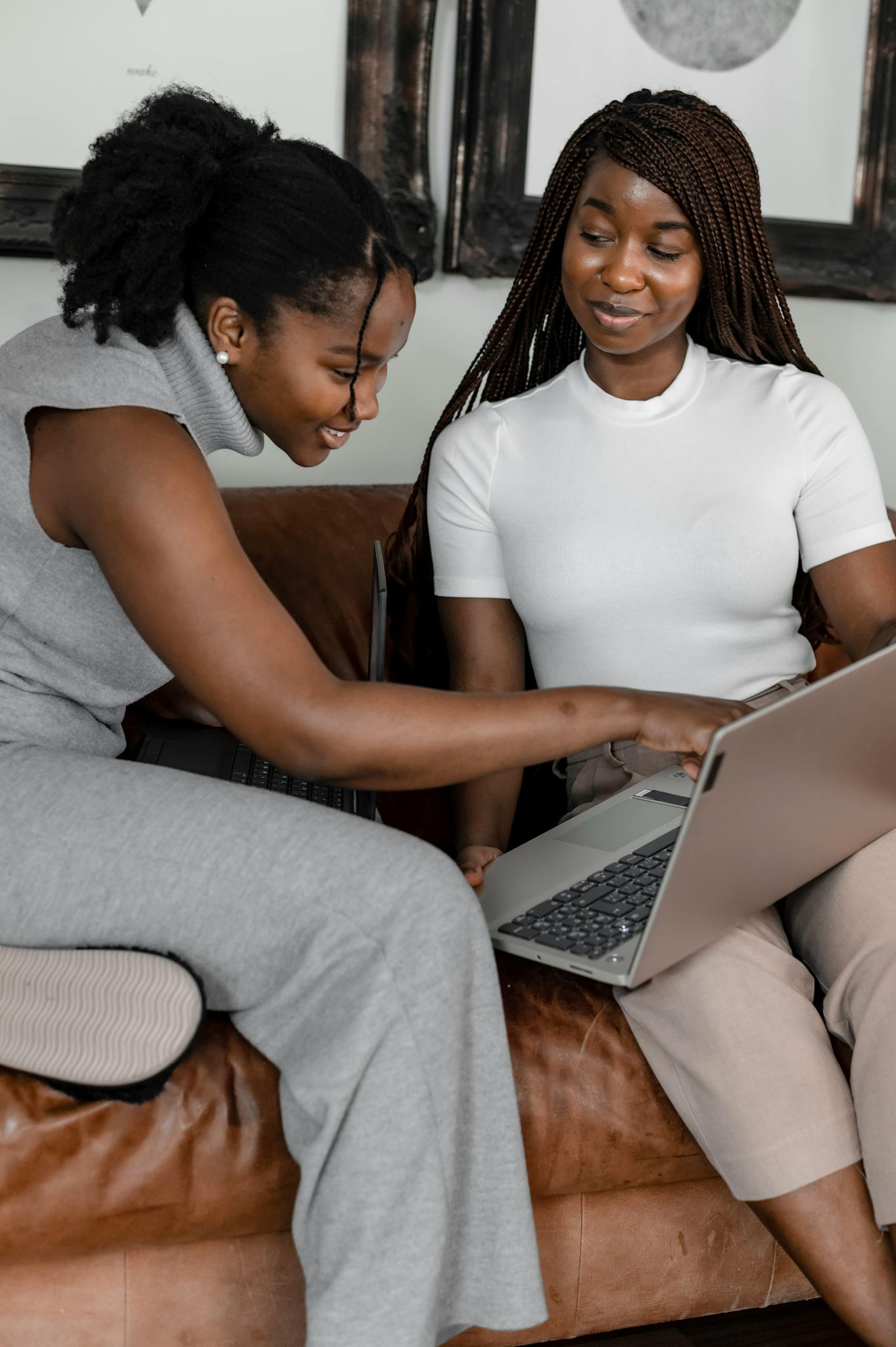 Two African American women smiling as they collaborate using a laptop indoors.